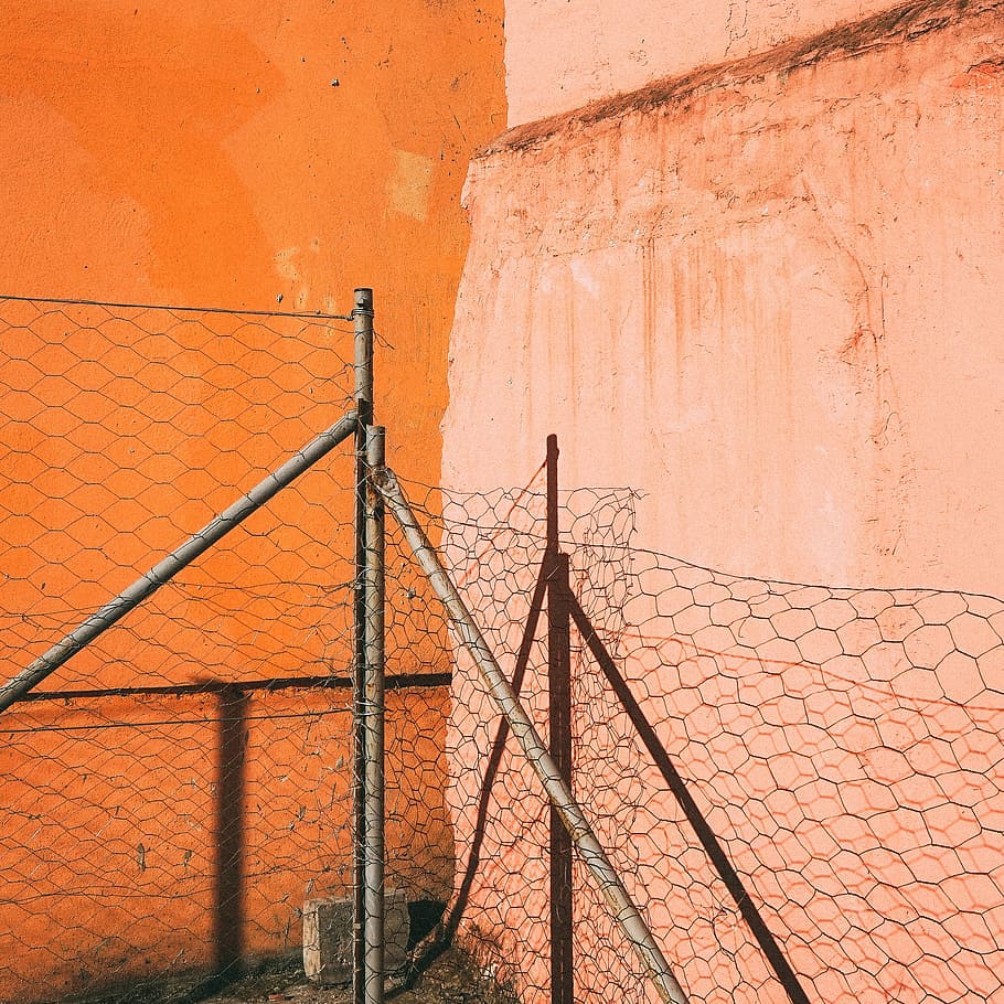 barbed wire on gray pipes near orange wall, gray cyclone fence near wall during daytime HD wallpaper