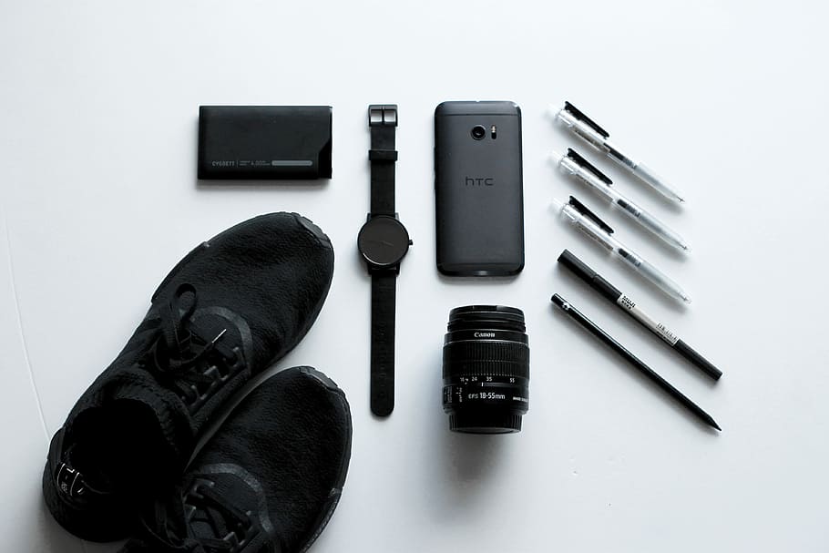 black HTC Android smartphone beside camera lens, ballpoint pens, and lace-up shoes, flat lay photography round black analog watch, HTC Android smartphone, and telephoto lens