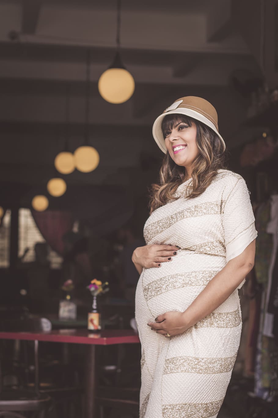 pregnant woman wearing white striped long-sleeved dress holding tummy and smiling