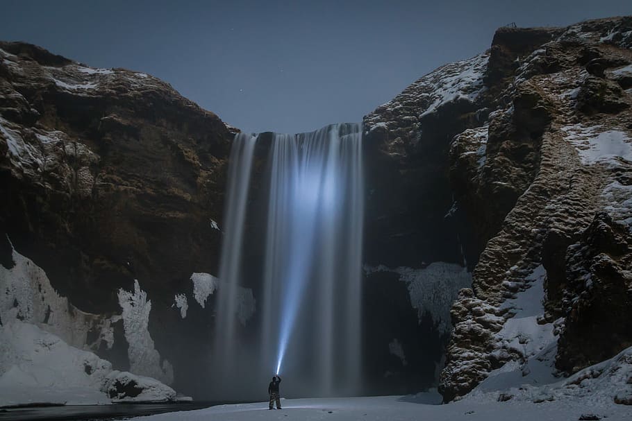 man standing in front of the waterfalls, man pointing flashlight toward waterfalls HD wallpaper
