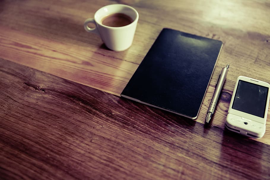 black notebook near click pen, white phone and white ceramic teacup with coffee HD wallpaper