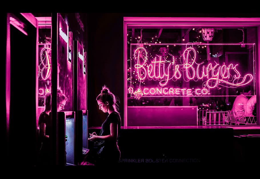 woman standing near glass window, woman standing beside Betty's Burger neon signage