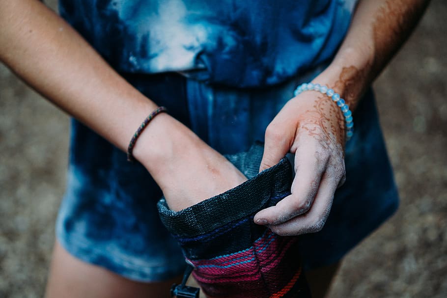 close-up photography of person holding black and pink pouch, person wearing blue shorts holding black and red pouch