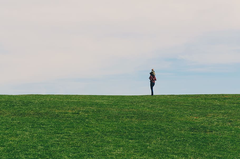 person standing on green grass field, person carrying child on back in green grass field during daytime HD wallpaper