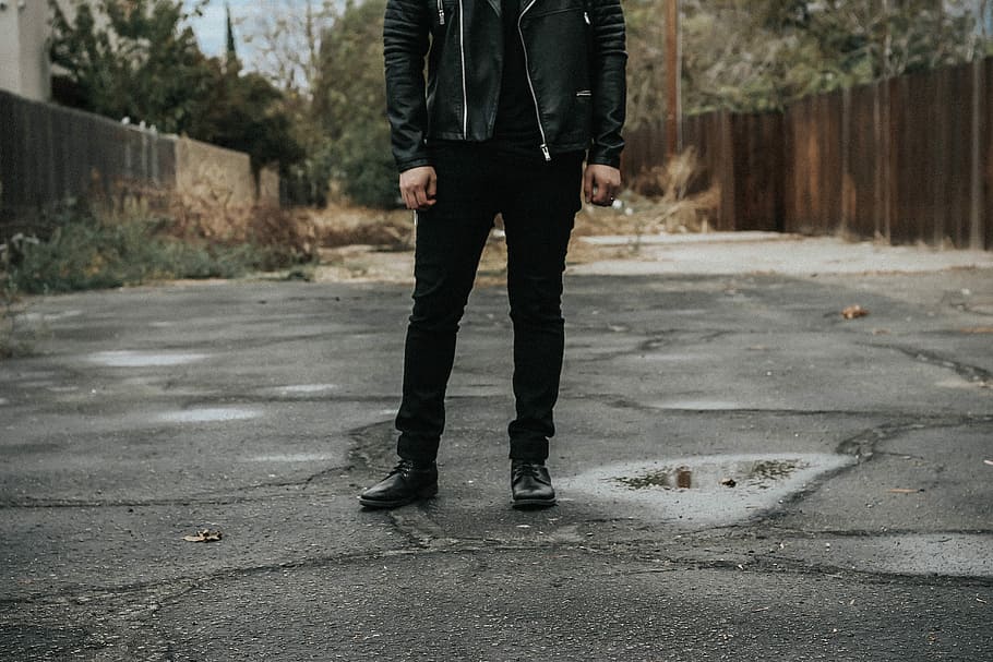 man wearing black pants standing on gray road, man wearing black jacket and pants standing between wooden fences HD wallpaper