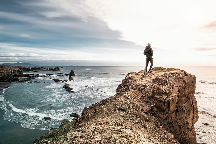 man on edge of cliff, man standing on cliff in front of sea, adventure