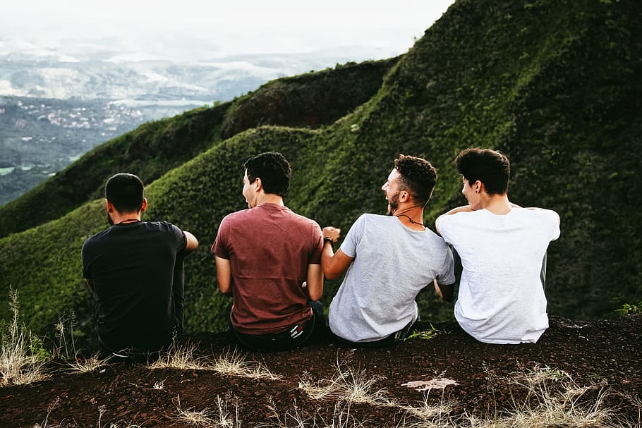 row of four men sitting on mountain trail, four men sitting on mountain cliff