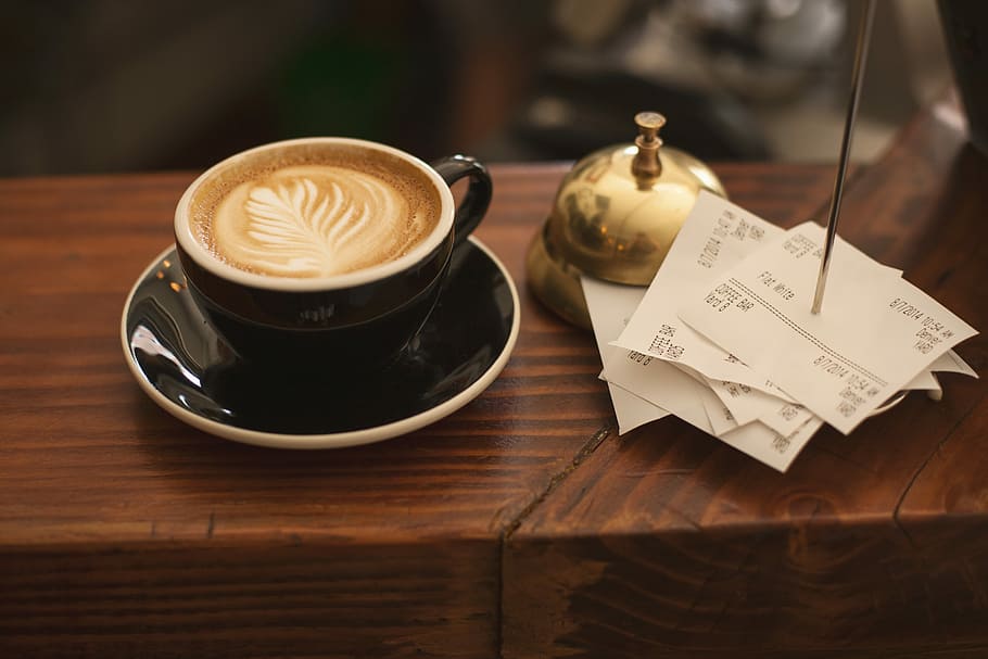 black ceramic cup with saucer and cappuccino on brown wooden surface, black and brown ceramic coffee mug beside gold steel bell HD wallpaper