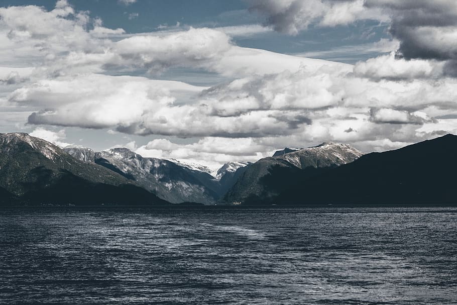 mountain near body of water under white skies at daytime, body of water near mountains under cloudy skies HD wallpaper