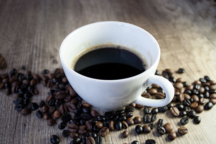 half-filled coffee in white ceramic teacup surrounded with coffee beans HD wallpaper
