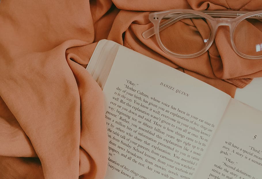 opened book page on top of pink mat near eyeglasses, opened Daniel Quinn book near brown textile and brown framed wayfarer-style eyeglasses HD wallpaper