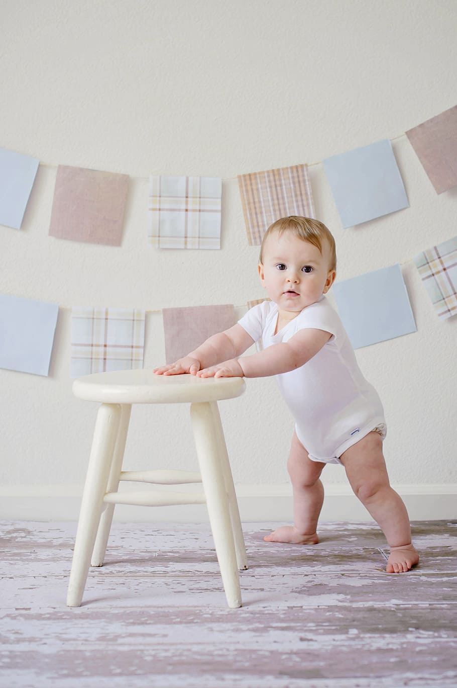 baby wearing white footsie holding into white wooden stool HD wallpaper