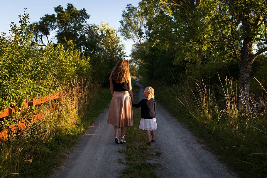 woman and girl walking on road surrounded by green grass, woman and girl walking on the street with many trees during daytime HD wallpaper
