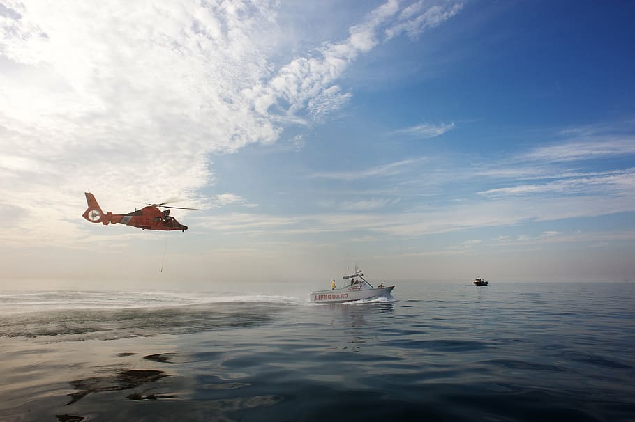 red helicopter above body of water with boat, coast guard, training