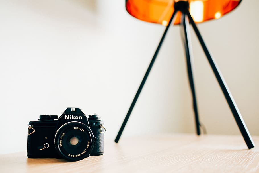 closeup photo of Nikon camera on wooden surface, black Nikon DSLR camera on table near table lamp HD wallpaper