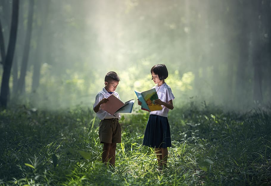girl and boy holding book while standing in grass field, children