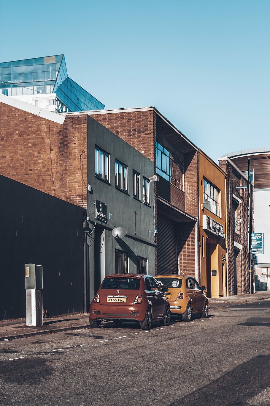 two hatchback beside wall, two red and yellow 3-door hatchbacks parked on roadside at daytime HD wallpaper