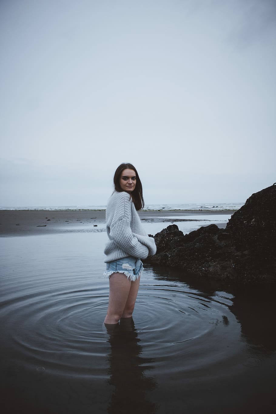 woman in gray sweater standing on shallow sea water under gray sky, woman in gray jacket on body of water HD wallpaper