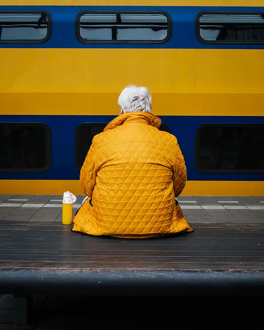 person wearing jacket and sitting on bench, person in yellow top sitting on bench in front of train HD wallpaper