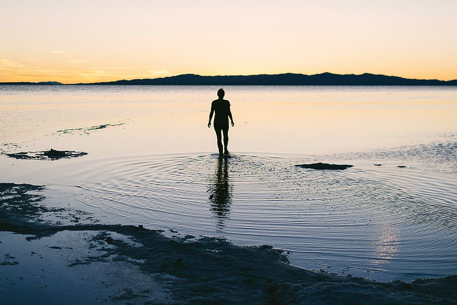 silhouette of person standing on body of water, silhouette photography of person on body of water