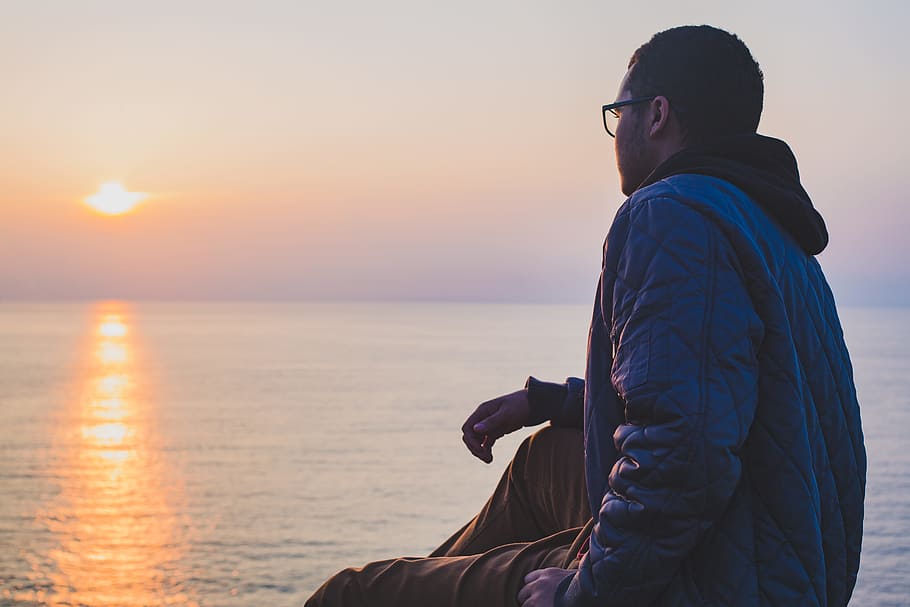 man sitting near body of water, man sitting near ocean during daytime HD wallpaper