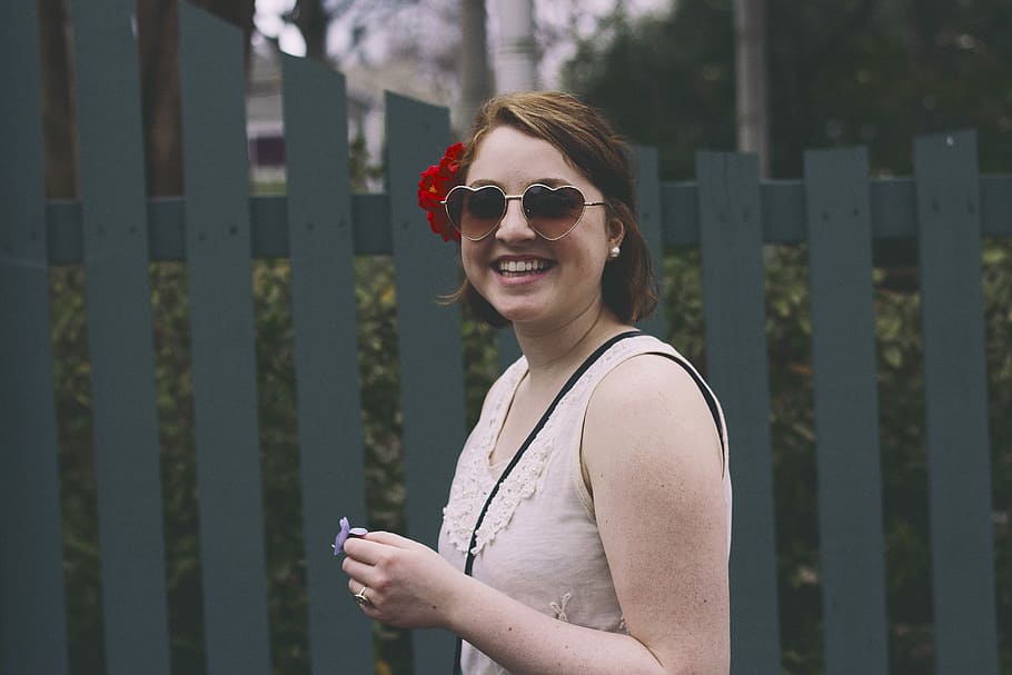 woman standing while smiling beside blue wooden fence, woman smiling near gray wooden fence