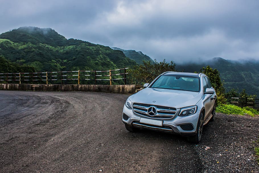 white Mercedes-Benz SUV parked near mountain under cloudy sky at daytime