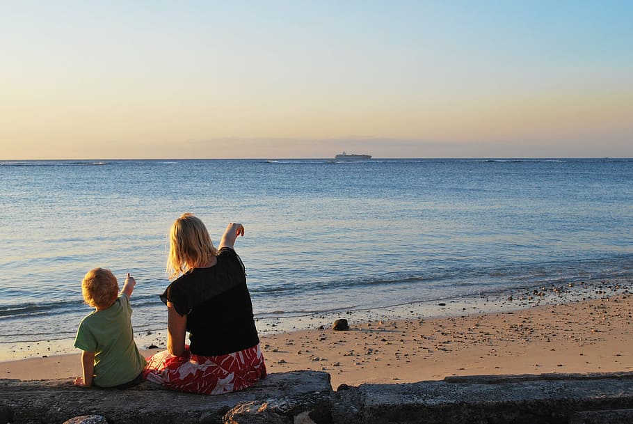 woman beside toddler sitting on concrete while pointing on beach HD wallpaper