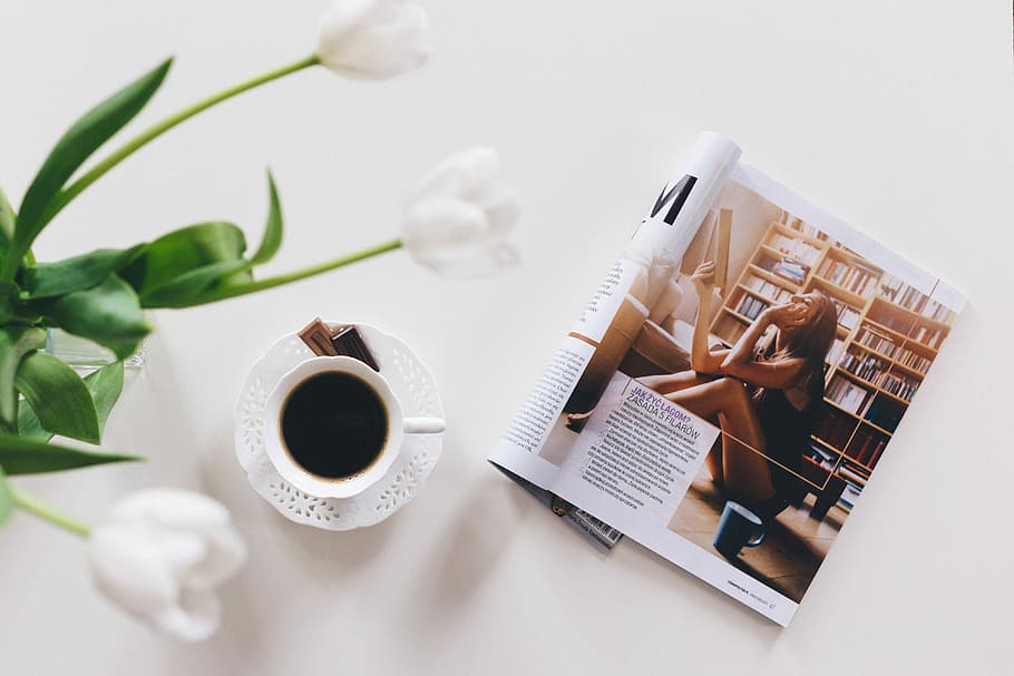 top view of opened magazine near up of coffee, white ceramic teacup and saucer near plant HD wallpaper
