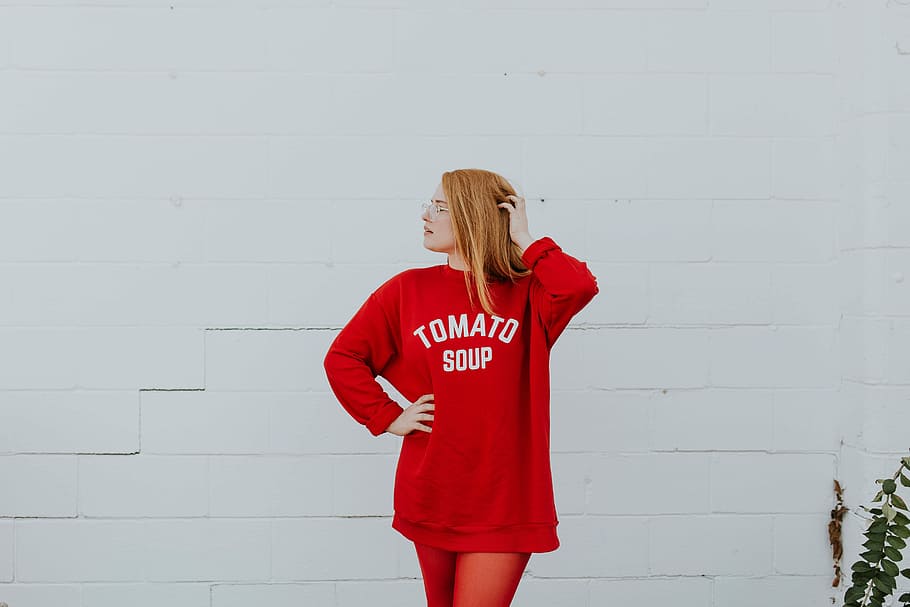woman in red Tomato soup printed jacket standing near white concrete wall with green leafy plant HD wallpaper