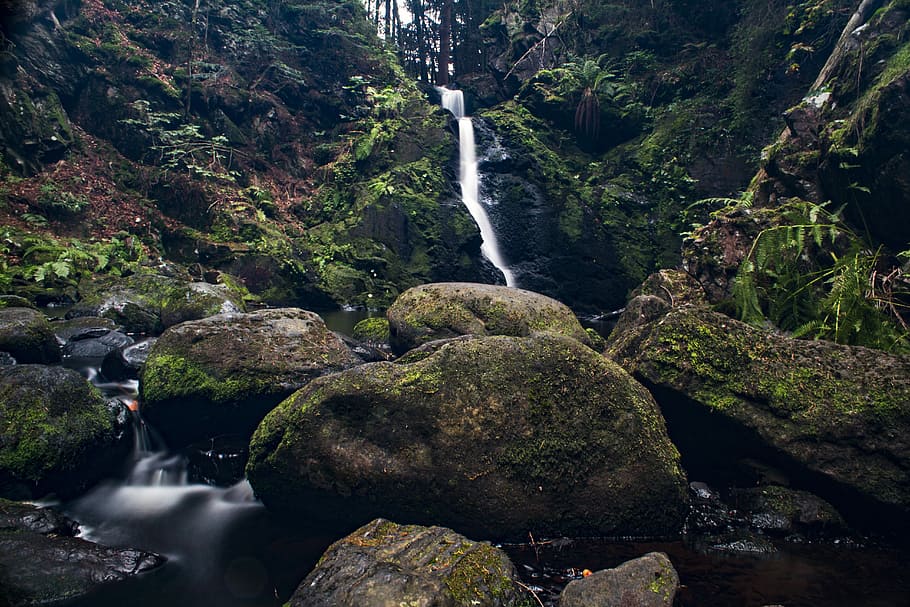 timelapse photo of waterfalls flowing between moss-covered stones and hills