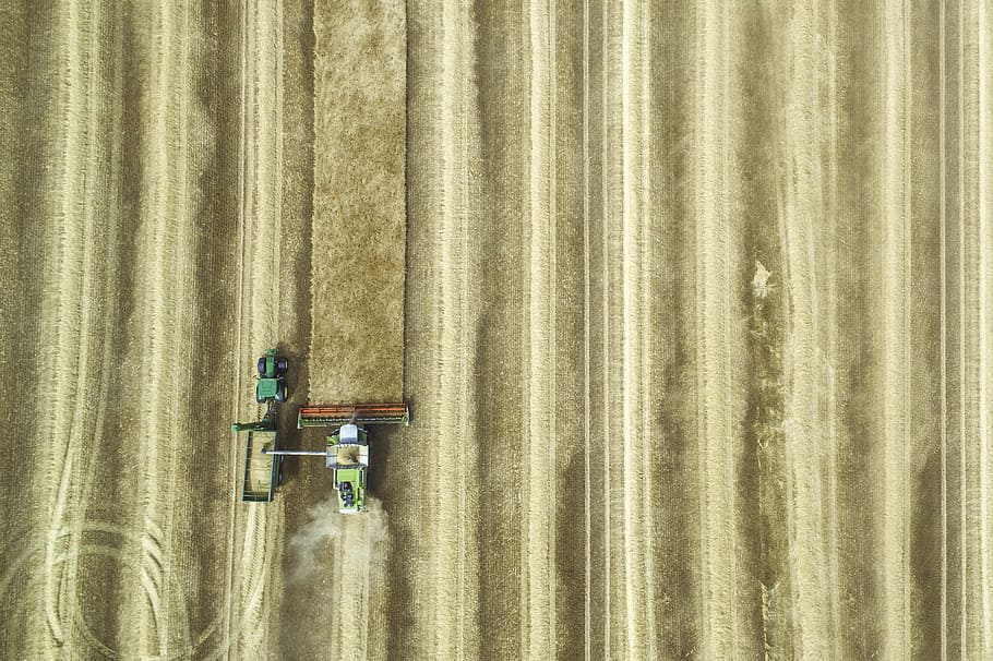 aerial view photography of tractor with disc harrow attachment on grass field, brown and black farm tractor