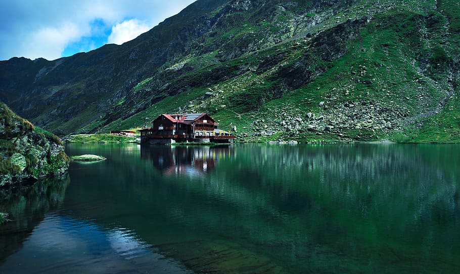 brown wooden house near mountain surrounded with water at daytime, house in the middle of water HD wallpaper