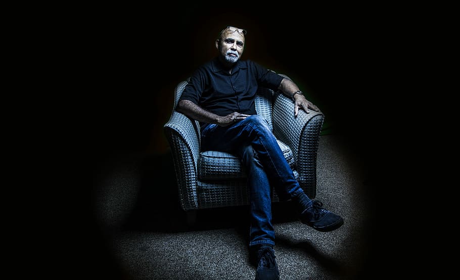 man sitting on sofa chair while crossing legs, person, dark, face