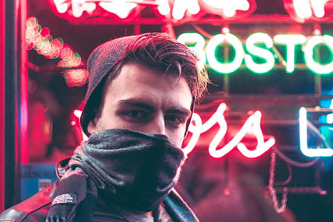 man with face half covered with mask standing in front of red and green neon light signage during daytime, man wearing gray and black scarf HD wallpaper
