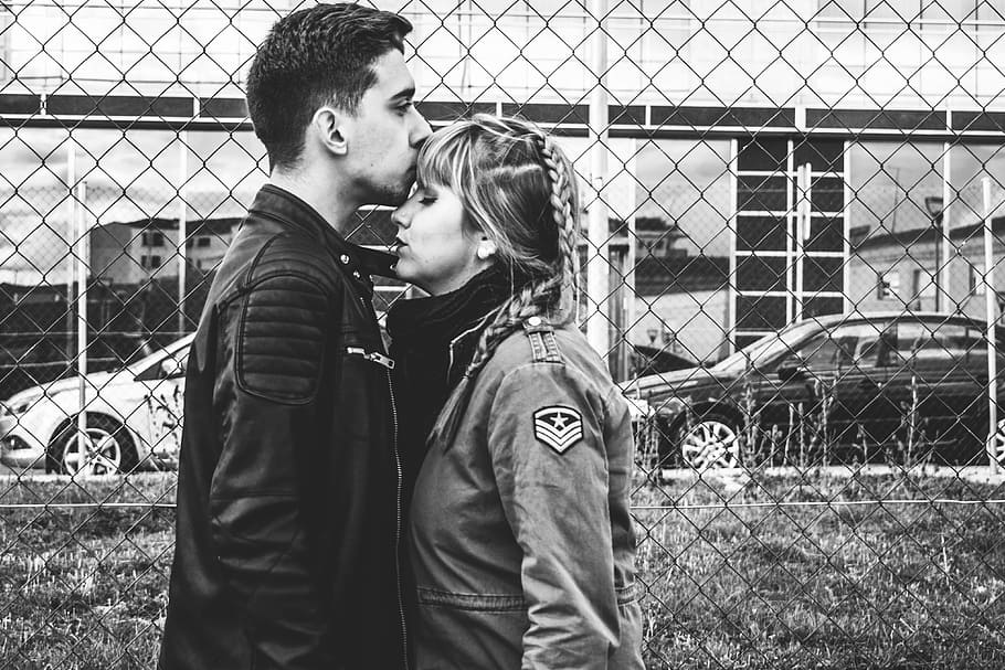 grayscale photo of man kissing forehead of woman near fence, grayscale photography of man kissing forehead of woman beside metal fence HD wallpaper