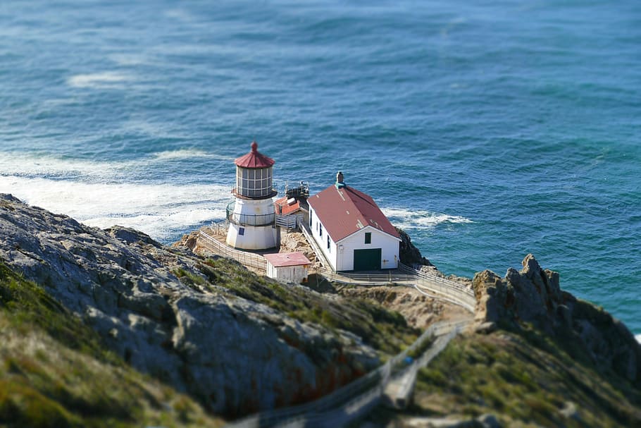 white and red house and lighthouse near sea at daytime, white and brown house beside lighthouse in front of ocean HD wallpaper
