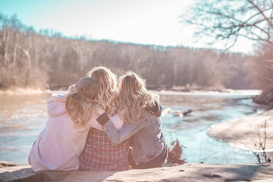 three women sitting on rock near body of water surrounded by trees during daytime, three woman sitting beside river HD wallpaper