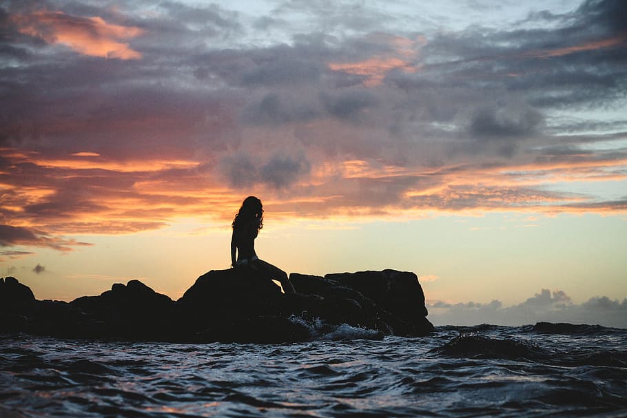 silhouette photo of woman sitting on rock during golden hour, silhouette of woman sitting on rock surrounded by body of water under gray sky at golden hour HD wallpaper