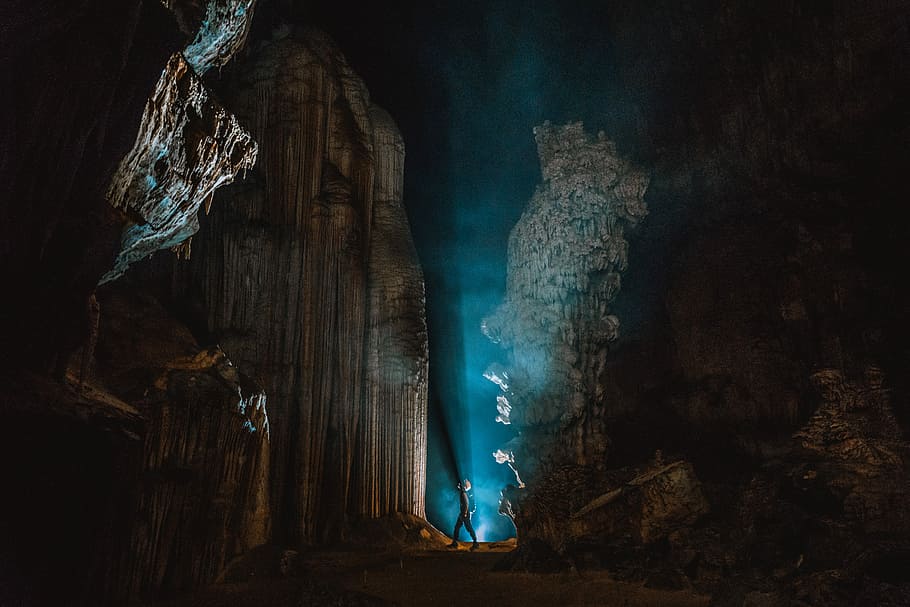 man standing near rock formation at night, person inside cave with blue light