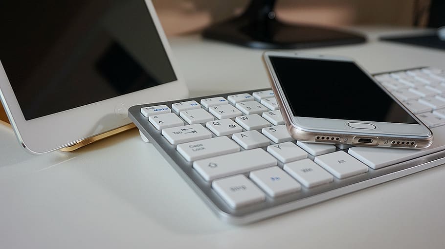 smartphone displaying black screen on wireless keyboard beside white iPad
