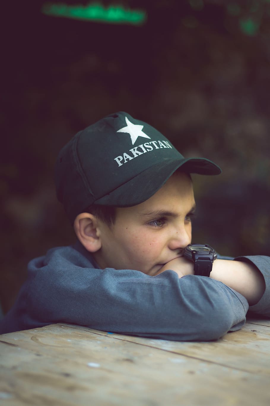 selective focus photography of boy leaning in front of brown wooden table, boy wearing black Pakistan cap, HD wallpaper