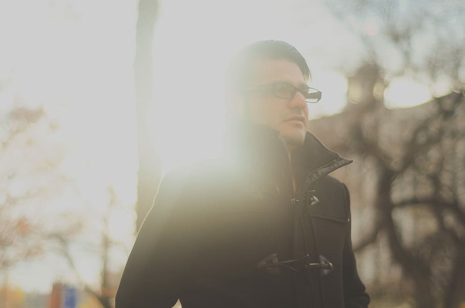man wearing eyeglasses and duffel jacket near trees during day HD wallpaper