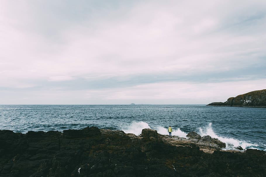 ocean waves near rock formation, person standing on rock formation surrounded by body of water during daytime HD wallpaper