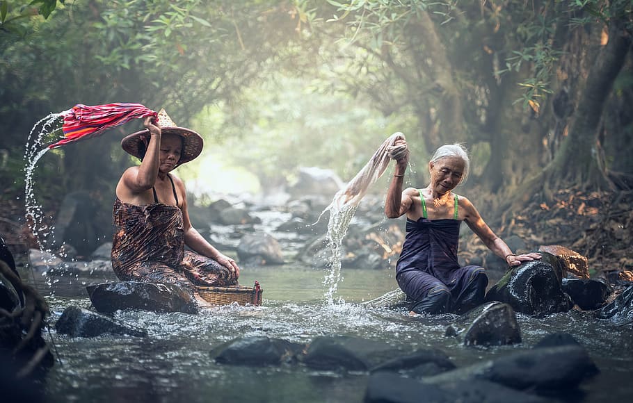 two sitting women on river washing clothes during daytime, asia