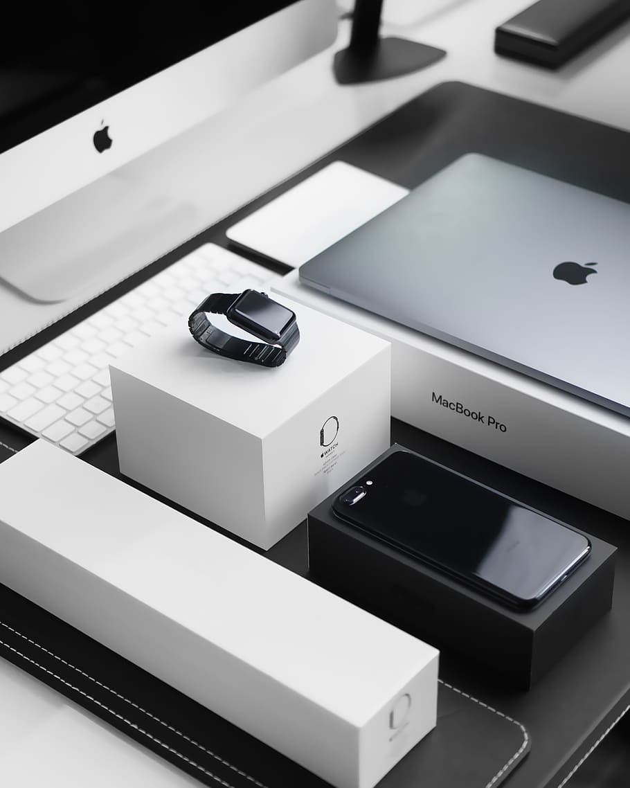 space black case Apple Watch, silver MacBook Pro, jet black iPhone 7 Plus, and silver iMac with corresponding boxes, black smartwatch near laptop