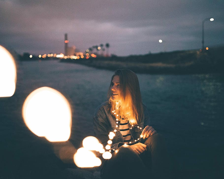 callah, smiling woman with string lights on her neck near body of water at nighttime HD wallpaper