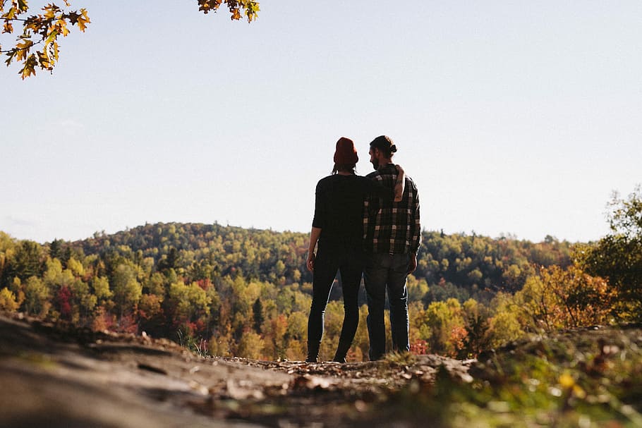 couple standing in front green trees field, man and woman in forest during daytime HD wallpaper