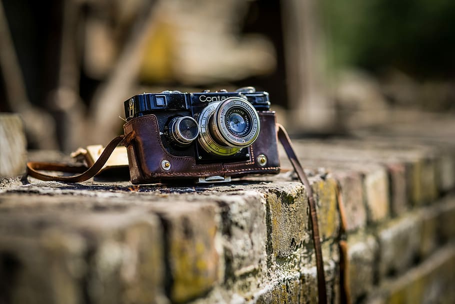 black SLR camera on brown brick surface, black and brown point-and-shoot camera on brown concrete fence