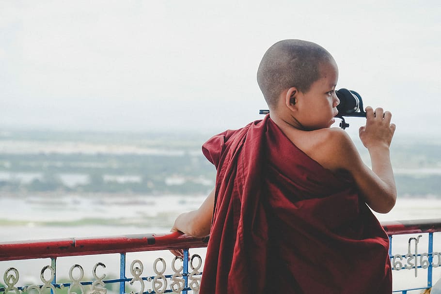 boy in red apparel leaning on blue and red metal railing during daytime, boy wearing red traditional dress standing in front of body of water HD wallpaper